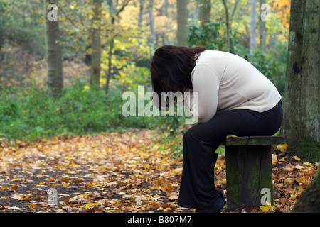 Premuto più di peso donna seduta sul banco in impostazione di bosco Foto Stock