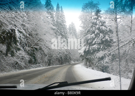 Il punto di vista di una coperta di neve la strada attraverso il parabrezza di un auto. Guida invernale su una coperta di neve strada rurale. Foto Stock