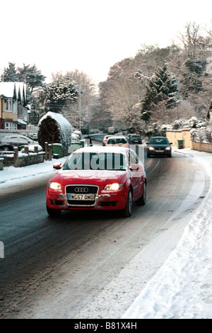 Un rosso Audi auto guidare lentamente il lungo Berkley Road, dopo una caduta di neve a Frome, Somerset, Inghilterra Foto Stock