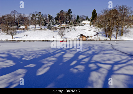 La luce del sole attraverso gli alberi crea ombre sul lago ghiacciato a Dunorlan Park a Tunbridge Wells dopo pesanti neve nel Regno Unito nel mese di febbraio 2009 Foto Stock