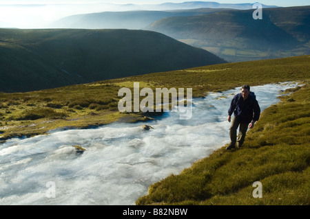 Un escursionista cammina davanti a una grande patch di ghiaccio in montagna nera Parco Nazionale di Brecon Beacons Powys Galles Centrale Regno Unito Europ Foto Stock