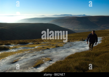 Un escursionista cammina davanti a una grande patch di ghiaccio in montagna nera Parco Nazionale di Brecon Beacons Powys Galles Centrale Regno Unito Foto Stock