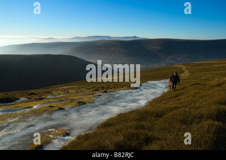 Un escursionista cammina davanti a una grande patch di ghiaccio in montagna nera Parco Nazionale di Brecon Beacons Powys Galles Centrale Regno Unito Europ Foto Stock