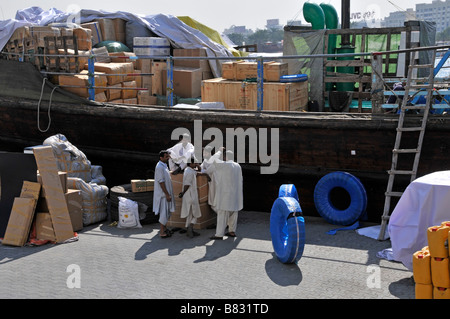 Persone del Dubai Creek che parlano accanto al carico del ponte sulla barca dhow Caricato con trasporto e merce sul porto banchina in United Emirati Arabi Uniti Medio Oriente Foto Stock