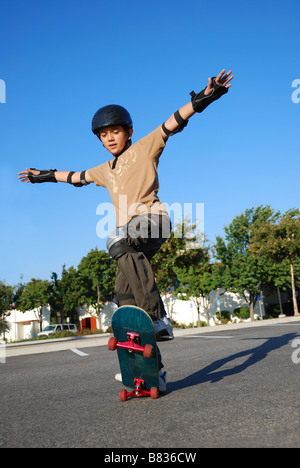 Ragazzo fare acrobazie su uno skateboard nel sole del pomeriggio con cielo blu in background Foto Stock