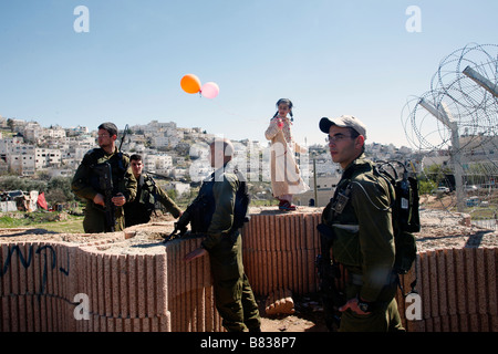 Soldati israeliani di guardia un colono israeliano ragazza durante la festa di Purim celebrazioni nella West Bank Settlement di Hebron. Foto Stock