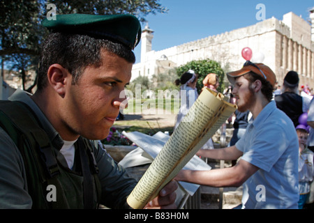 Poliziotto israeliano la lettura di un testo religioso durante la festa di Purim celebrazioni a Hebron. Foto Stock