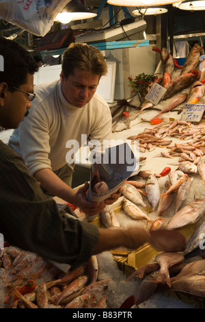 Pesce fresco e prelibatezze di mare punto di vista mediterraneo; il venditore impacca un pesce, il compratore ottiene i suoi beni dal venditore, mercato centrale di Atene, Grecia Foto Stock