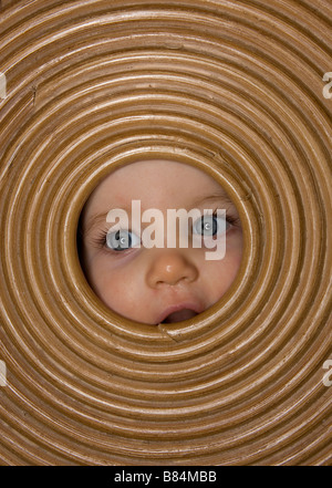 Un bambino con lunghe ciglia guardando attraverso un cesto per la biancheria coperchio Foto Stock