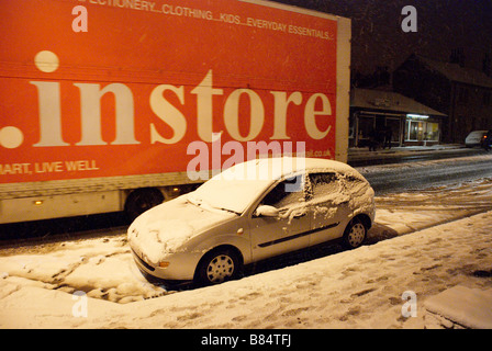 Autocarro passando una macchina parcheggiata su una strada innevata Foto Stock