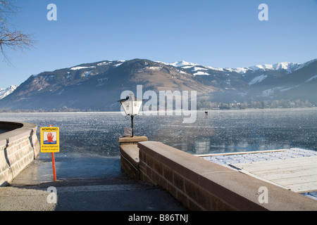 Zell am See Austria UE gennaio cartelli di avvertimento a non camminare sulla congelati lago Zeller See con due uomini controllo della profondità del ghiaccio Foto Stock