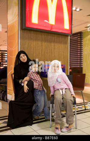 Madre musulmana e i bambini di fronte a McDonald's ristorante nella sala partenze dell'aeroporto internazionale di Bahrain. Foto Stock