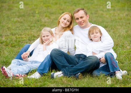 Famiglia sedersi sull'erba felicemente close up ritratto Foto Stock