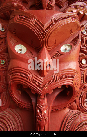 Un intaglio Maori di una faccia con la lingua fuori e gli occhi aperti su un marae sala riunioni in Waitangi Treaty Grounds Foto Stock