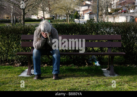 Foto di stock di una donna seduta da sola su una panchina nel parco con la sua testa con le mani Foto Stock