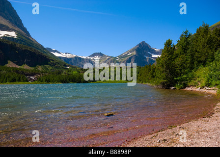 Le onde lentamente in rotolamento su una piccola spiaggia rocciosa in molti ghiacciaio con sullo sfondo le montagne con la neve eterna Foto Stock