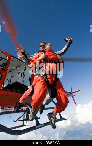 Tandem Skydive in uscita da un elicottero nel cielo blu e iniziare a tuffarsi in caduta libera collegati insieme come un giovane subacqueo Foto Stock