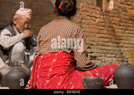 Il vecchio uomo nepalese e pot venditore in abiti tradizionali con il cappello si siede di fumare narghilè tubo con donna all'aperto sulla strada a Bhaktapur città vecchia, Nepal Foto Stock