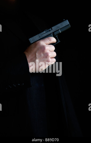 Vista laterale di una mano di un uomo in possesso di una pistola. Sfondo nero. Foto Stock