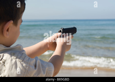 Giovane ragazzo puntando con pistola giocattolo al mare Foto Stock