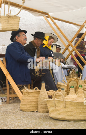 Gli artigiani in costume tradizionale cesti che fanno fuori di sparto presso la tradizionale fiera di artigianato, Santa Eulalia, Ibiza, Spagna. Foto Stock