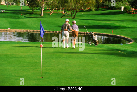 I cittadini anziani a piedi spento verde insieme durante il round di golf in Palm Springs, California Foto Stock