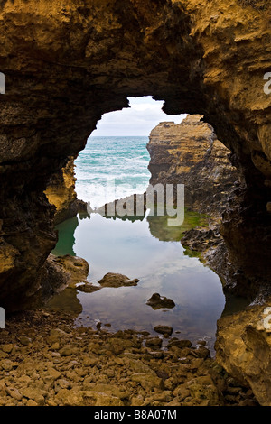 Una roccia piscina e vista attraverso una apertura di roccia verso l'oceano in Australia Great Ocean Road Foto Stock