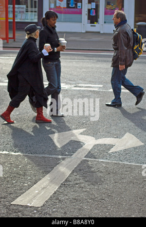 Tre pedoni che attraversano una strada con la segnaletica stradale le frecce che puntano in due direzioni, a Chiswick, a ovest di Londra - Inghilterra Foto Stock