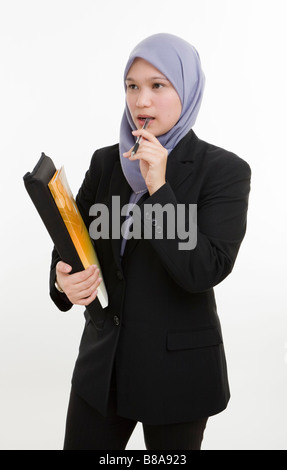 Executive donna musulmana contro uno sfondo bianco in piedi tenendo la cartella mordere di penna e di pensiero. Foto Stock