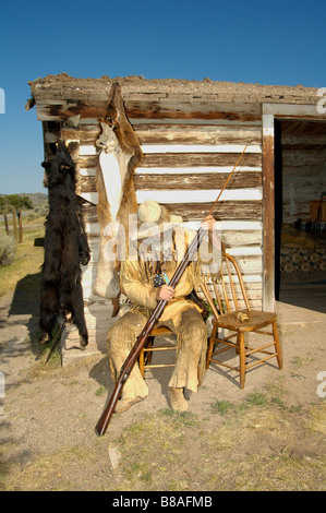 Una scena nella città fantasma di Nevada City Montana un orso hunter pulisce la sua pistola mentre è seduto al di fuori del suo log cabin Foto Stock