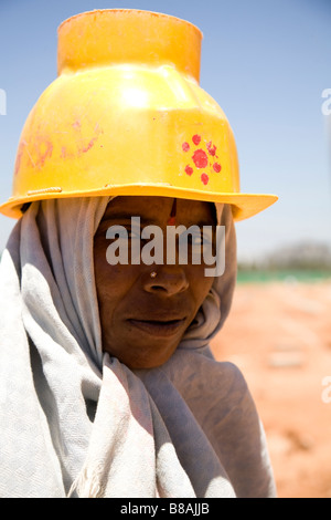 Una donna in giallo casco di sicurezza funziona su un sito in costruzione a Bangalore in India. Foto Stock