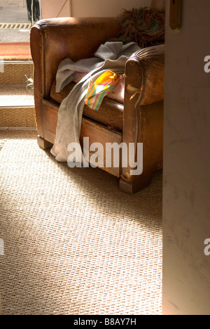 Guardando attraverso una porta a una vista ritagliata della vecchia poltrona in pelle con sciarpe su di esso Foto Stock