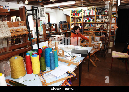 Due tessitori a mano lavorando a piccoli in legno tradizionali macchine di tessitura in un piccolo studio di tessili nel Regno Unito in fabbrica Foto Stock