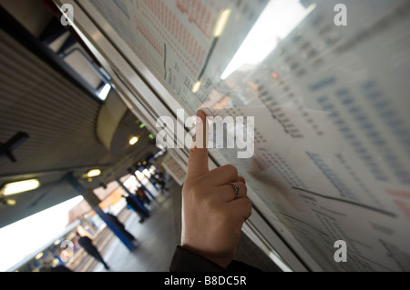 Una femmina di passeggero in una stazione ferroviaria puntando il dito sull'orario di partenza sulla piattaforma England Regno Unito Foto Stock