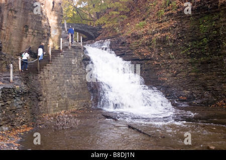 Sentiero per cascate Cascadilla Creek Gorge a Ithaca, New York, con escursionisti su scale di pietra accanto a una cascata e un ponte panoramico in pietra. Foto Stock