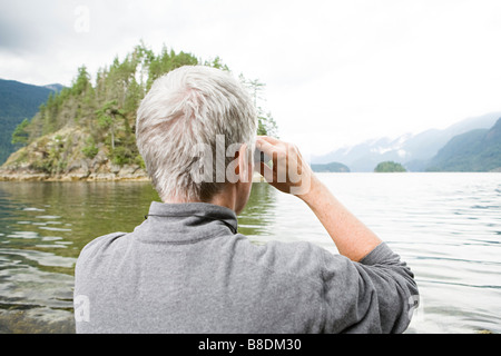 Uomo che guarda un fiordo con il binocolo Foto Stock