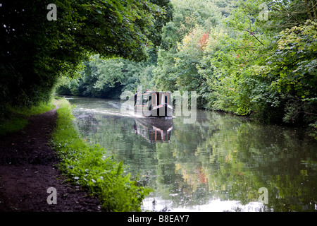 Due uomini sterzare una stretta barca lungo la Bridgewater Canal e negoziare un divario in termini di alberi dove un albero di luce che cade Foto Stock