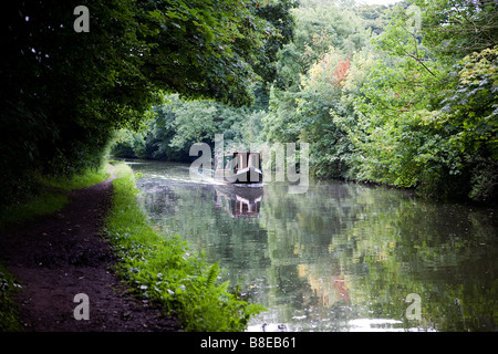 Due uomini sterzare una stretta barca lungo la Bridgewater Canal e negoziare un divario in termini di alberi dove un albero di luce che cade Foto Stock