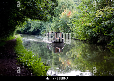 Due uomini sterzare una stretta barca lungo la Bridgewater Canal e negoziare un divario in termini di alberi dove un albero di luce che cade Foto Stock