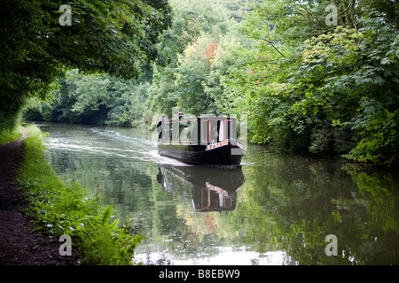 Due uomini sterzare una stretta barca lungo la Bridgewater Canal e negoziare un divario in termini di alberi dove un albero di luce che cade Foto Stock