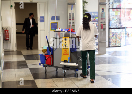 Donna delle pulizie a piedi attraverso la sala di attesa all'aeroporto di Monaco di Baviera, Germania Foto Stock