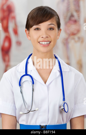 Un bel giovane infermiere con uno stetoscopio girato in un ospedale con anatomia umana i grafici al di fuori della messa a fuoco dietro di lei Foto Stock