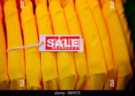 Il bianco e il rosso vendita segno su una fila di magliette di colore giallo Foto Stock