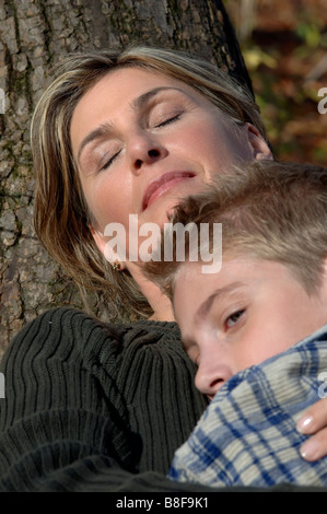 Donna appoggiata contro un albero e abbracciando il suo figlio Foto Stock