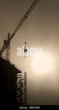 Unnidentifiable sito in costruzione stagliano contro il sun. Il sollevamento con gru attrezzature. Foto Stock