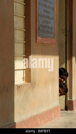 Due ragazzi indiani spuntano fuori dalla porta della scuola Foto Stock