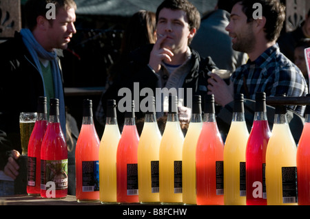 Hackney East London Broadway Market .Il succo di mela in vendita di fronte a uomini di bere birra al di fuori del pub di sabato. Foto Stock