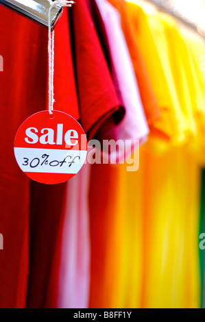 Il bianco e il rosso segno sconto pendente da una maglietta di fronte a una fila di colorati T shirt Foto Stock