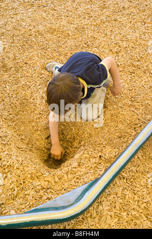Elevato angolo di visione di 6 anno vecchio ragazzo scavando nel parco giochi contenenti trucioli di legno Foto Stock