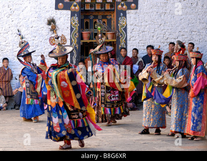 Un pubblico bhutanesi in contesti formali nazionali Orologi vestito come musicisti accompagnano un black hat danzatrice presso il festival Trashigang. Foto Stock